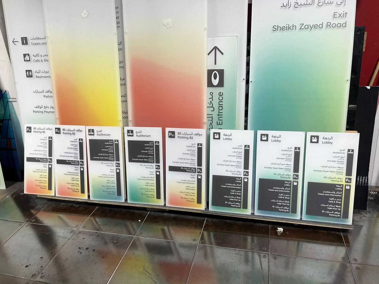 A set of bilingual Arabic and English wayfinding panels in the studio, printed with pictograms and directional listings for lobby, auditorium and parking levels