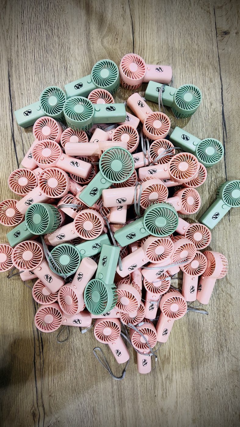 A pile of pink and mint mini handheld fans, each printed with a client logo