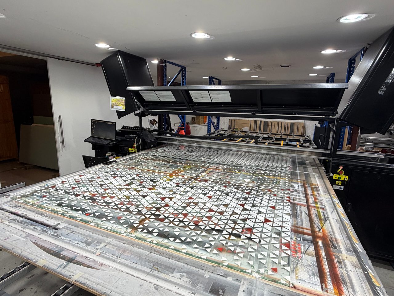 A run of large printed glass panels seen from the corner of the flatbed, a white and red triangle pattern with clear glass left between the shapes
