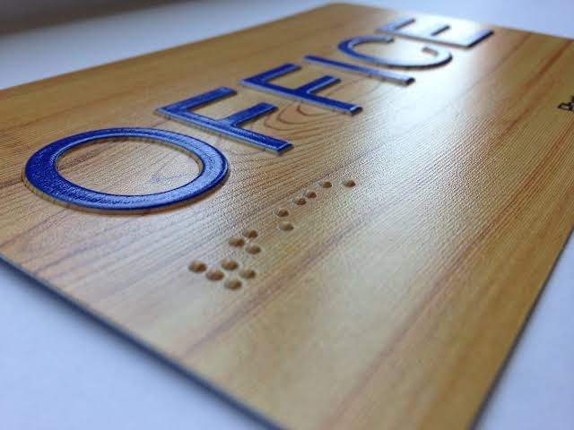 Braille office sign in a wood finish, with raised metallic blue OFFICE lettering and a row of tactile braille dots