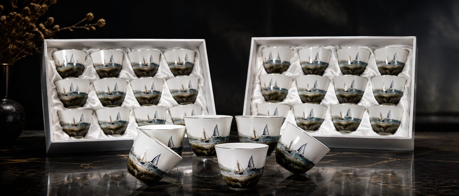 Boxed sets of porcelain qahwa cups printed with a coastal sailing scene and gold rims