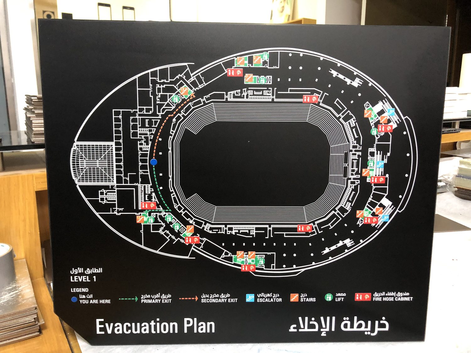 A black panel printed with a bilingual evacuation plan and icon legend, propped on the workbench