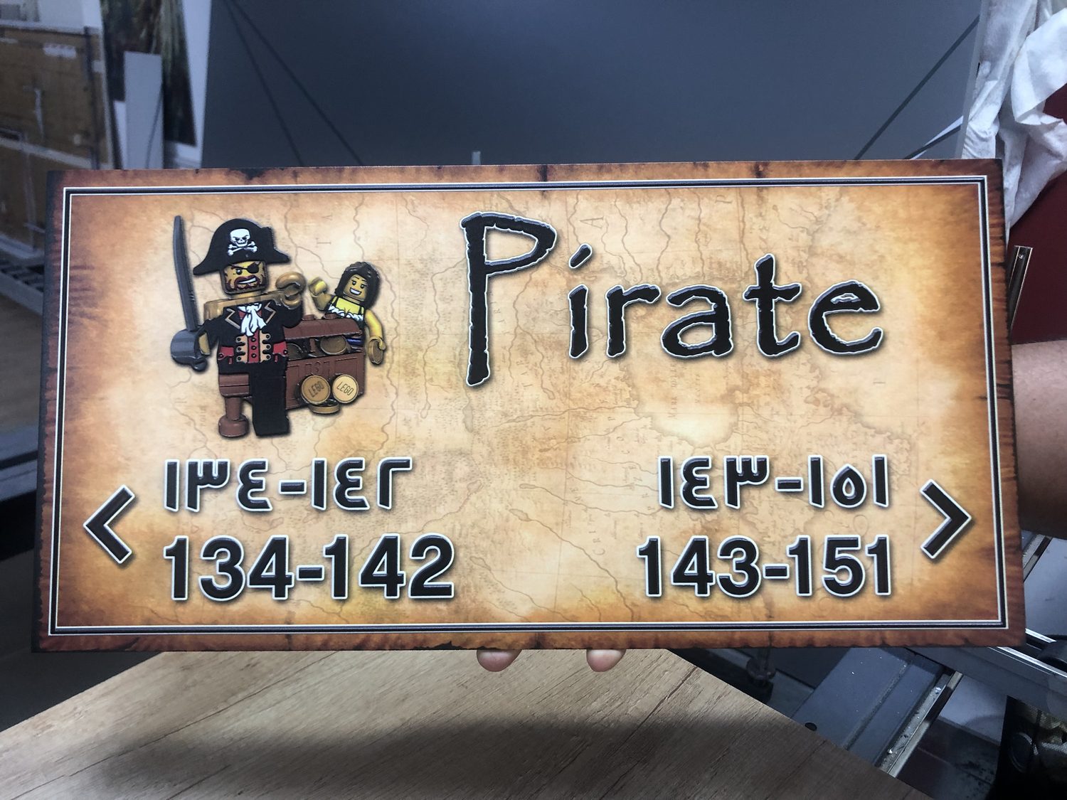 A hand-held directional sign printed edge to edge with a treasure-map design and fine bilingual type