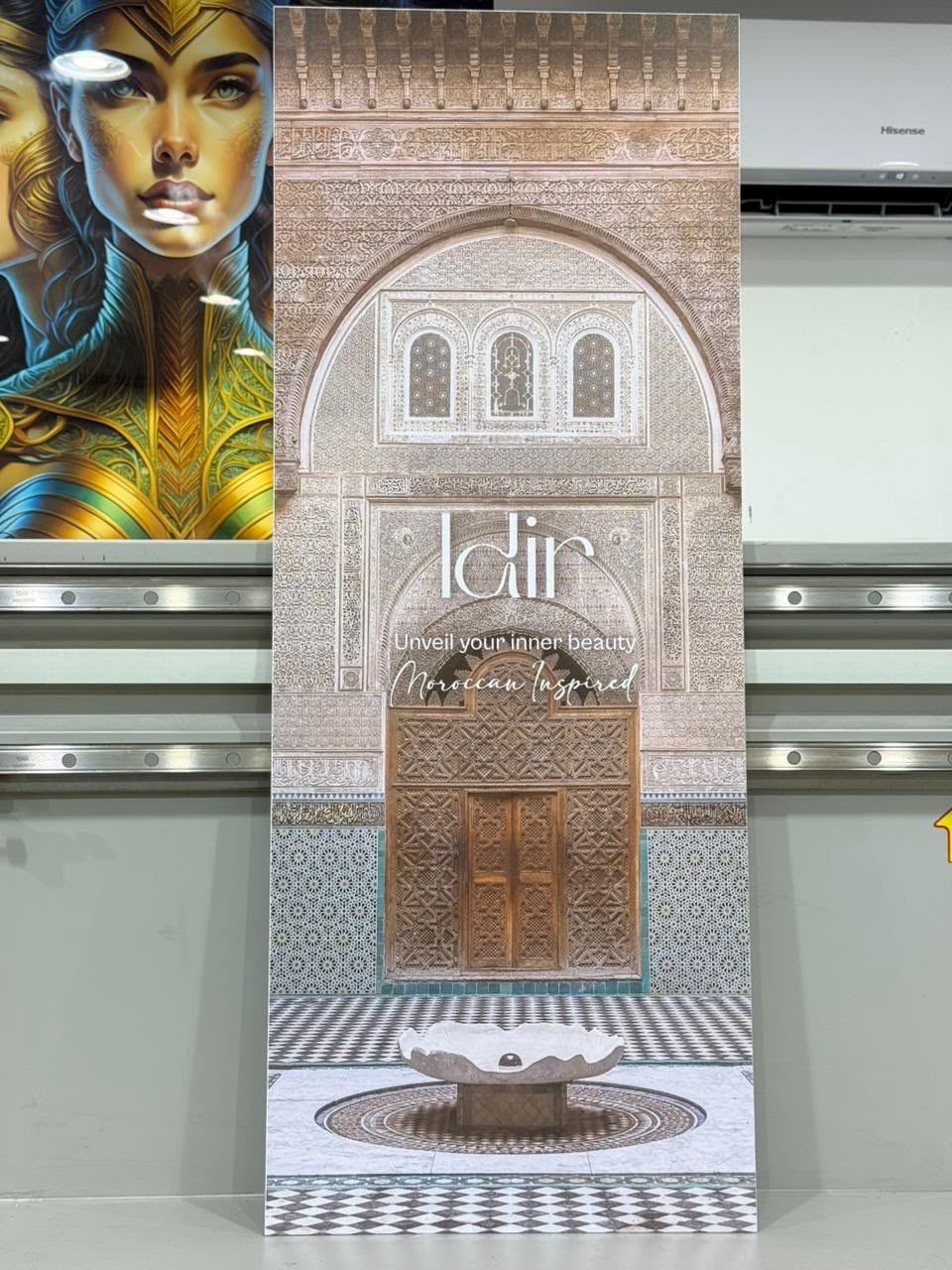 A tall display board printed edge to edge with a Moroccan courtyard photograph, standing in the workshop